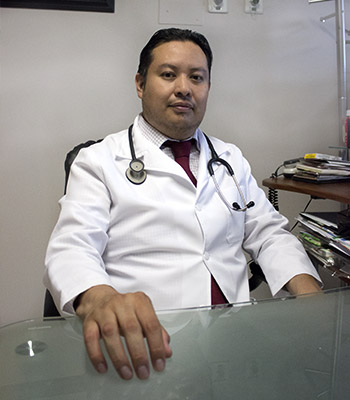 Dr. Emmanuel Sandoval sentado con bata blanca y un estetoscopio colgando de su cuello